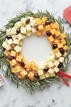 a wreath made out of cheese and olives on a marble counter top with utensils