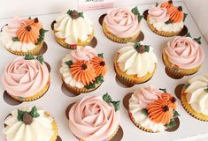 cupcakes with pink frosting and orange flowers on them are displayed in a box