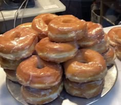 a pile of glazed donuts sitting on top of a silver plate