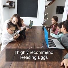 a group of children sitting at a table with laptops and books in front of them