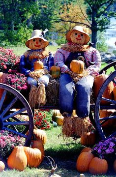 two scarecrows sitting on top of a wagon filled with pumpkins