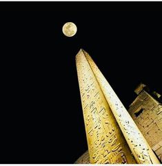 an image of the moon setting behind some buildings in egypt, with writing on it's spires