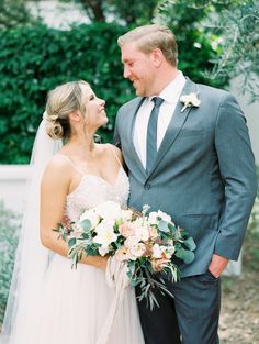 a bride and groom standing together in front of trees