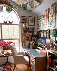 a room with lots of pictures on the wall and a desk in front of a window