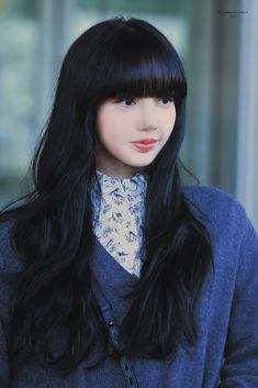 a woman with long black hair wearing a blue sweater and flowered collar shirt is looking at the camera