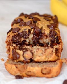 a loaf of chocolate chip banana bread on top of a paper towel next to two bananas