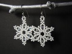 white beaded snowflake earrings hanging from a branch on a black background,