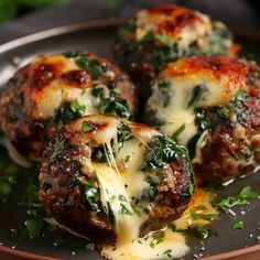 three stuffed meatballs covered in cheese and spinach on a plate with parsley