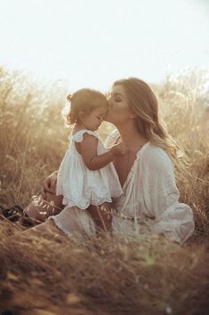 a woman sitting in the grass kissing a small child