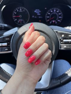 a woman's hand on the steering wheel of a car with red nail polish