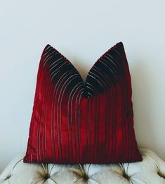 a red pillow sitting on top of a white chair next to a wall with a black stripe