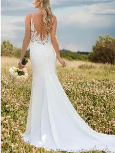 a woman in a white wedding dress standing in a field with her back to the camera