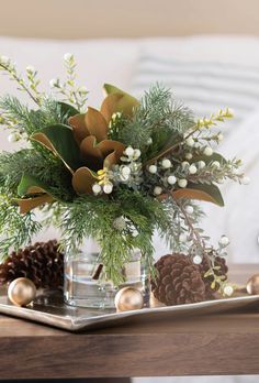 a glass vase filled with flowers and greenery on top of a table next to pine cones