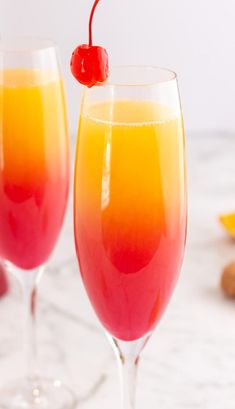 two wine glasses filled with liquid and topped with a cherry garnish, sitting on a marble surface