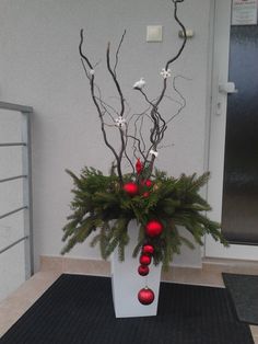 a white vase filled with christmas decorations on top of a black mat next to a door