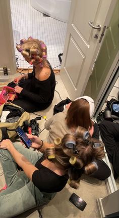 two women sitting on the floor with hairdryers in their hands and one woman holding a cell phone