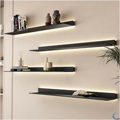 three black shelves with lights above them in a living room or dining room, along with bookshelves and vases on the wall