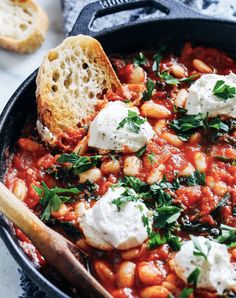 a skillet filled with lots of food on top of a white tablecloth next to bread