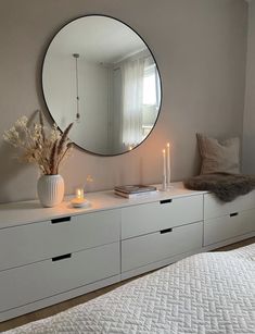 a bedroom with a large round mirror on the wall next to a white dresser and bed