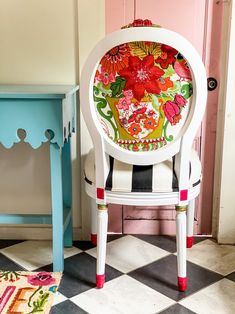 a white chair with flowers painted on it next to a blue table and pink door