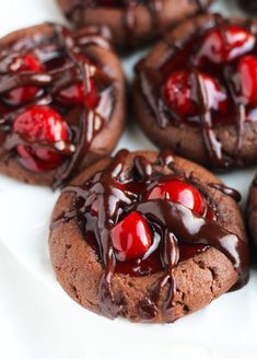 chocolate cookies with cherries are on a white plate and drizzled with chocolate