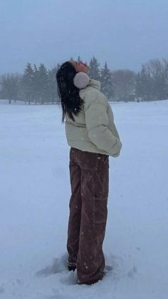 a woman standing in the snow with her back turned to the camera, wearing brown pants and a white jacket