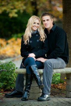 a young man and woman sitting on a bench in the fall with their arms around each other