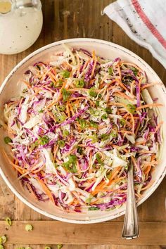 a white bowl filled with coleslaw on top of a wooden cutting board next to a spoon