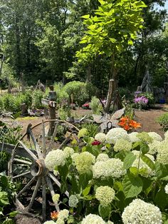 a garden with lots of flowers and an old wagon in the middle, surrounded by greenery