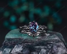 a ring with a blue stone in the center on top of a rock, surrounded by green leaves