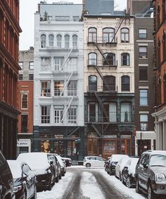 cars are parked on the street in front of buildings with snow all over them and stairs going up