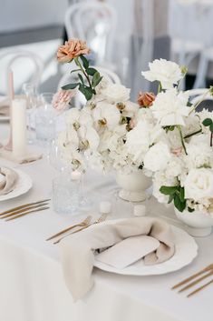 the table is set with white flowers and silverware