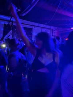 a group of people dancing in a dark room with blue lights on the ceiling and one woman holding her arm up