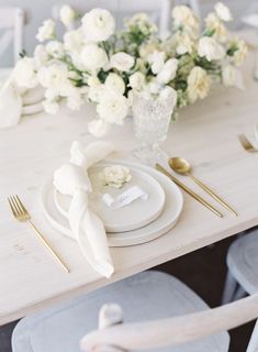 a table set with plates, silverware and white flowers in vases on it