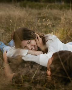 two people laying in the grass with their heads on each other's shoulders and smiling