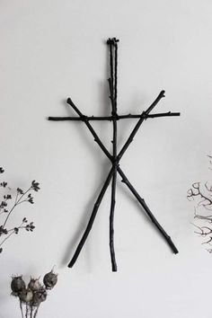 a cross made out of sticks on the wall next to some dead flowers and branches