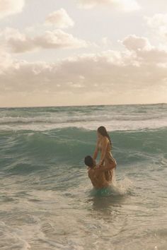 two people standing in the ocean with one person on his back and another holding him up