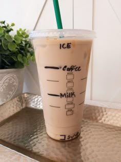 a cup with a straw in it sitting on a tray next to a potted plant