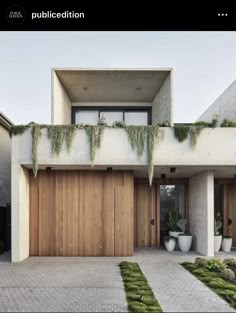 a modern house with wooden garage doors and green plants on the roof, along with brick walkway