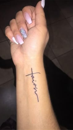 a woman's arm with a cross tattoo on it and the word faith written in cursive font