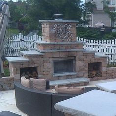 an outdoor fireplace is built into the side of a patio with chairs and tables around it