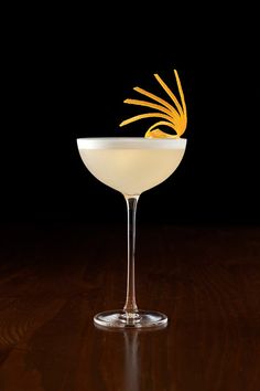 a glass filled with a drink on top of a wooden table next to a black background