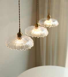 three glass lights hanging from a ceiling in a room with white walls and drapes