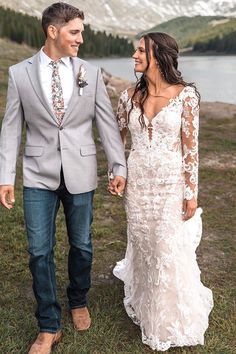 a bride and groom holding hands in front of a mountain lake