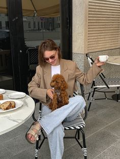 a woman sitting in a chair holding a brown dog and eating some food from a plate