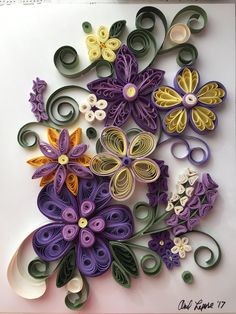 paper quilled flowers are arranged on a white surface with green, yellow and purple ribbons