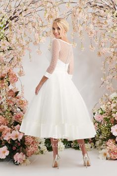 a woman wearing a white dress and heels standing in front of a floral arch with pink flowers