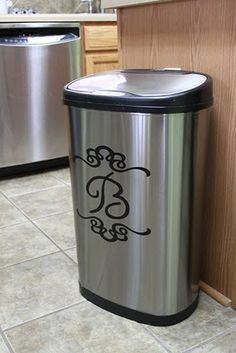 a stainless steel trash can with the letter b on it next to a dishwasher