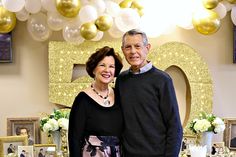 a man and woman standing in front of a table with balloons on the wall behind them