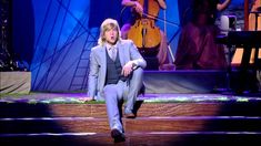 a man in a suit and tie is sitting on the stage with his legs crossed